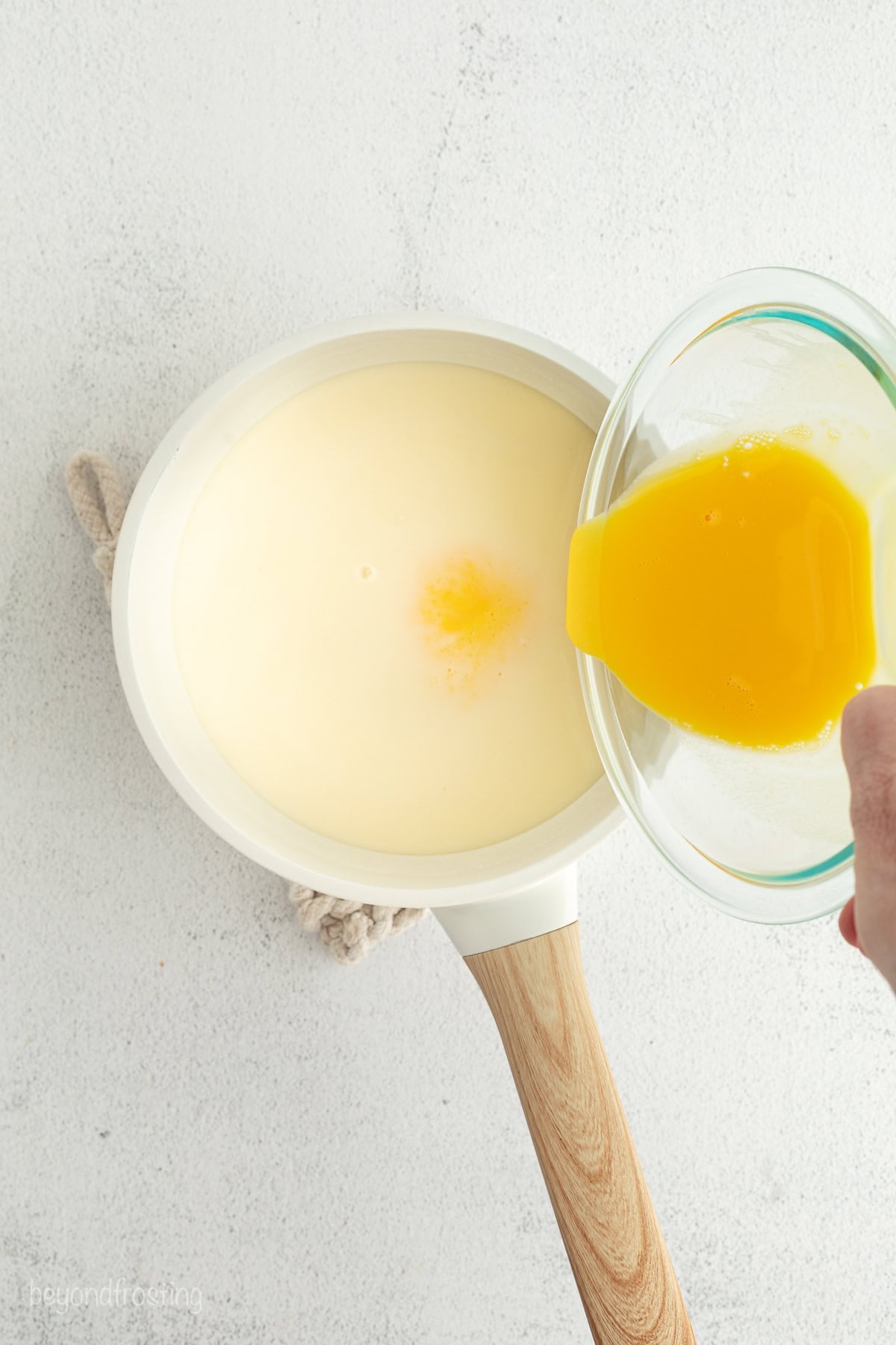 Make the best no-bake banana pudding cheesecake with creamy cheesecake filling, fresh banana slices, homemade pudding, and whipped cream. Pouring the tempered eggs into the warm milk mixture to make the pudding.
