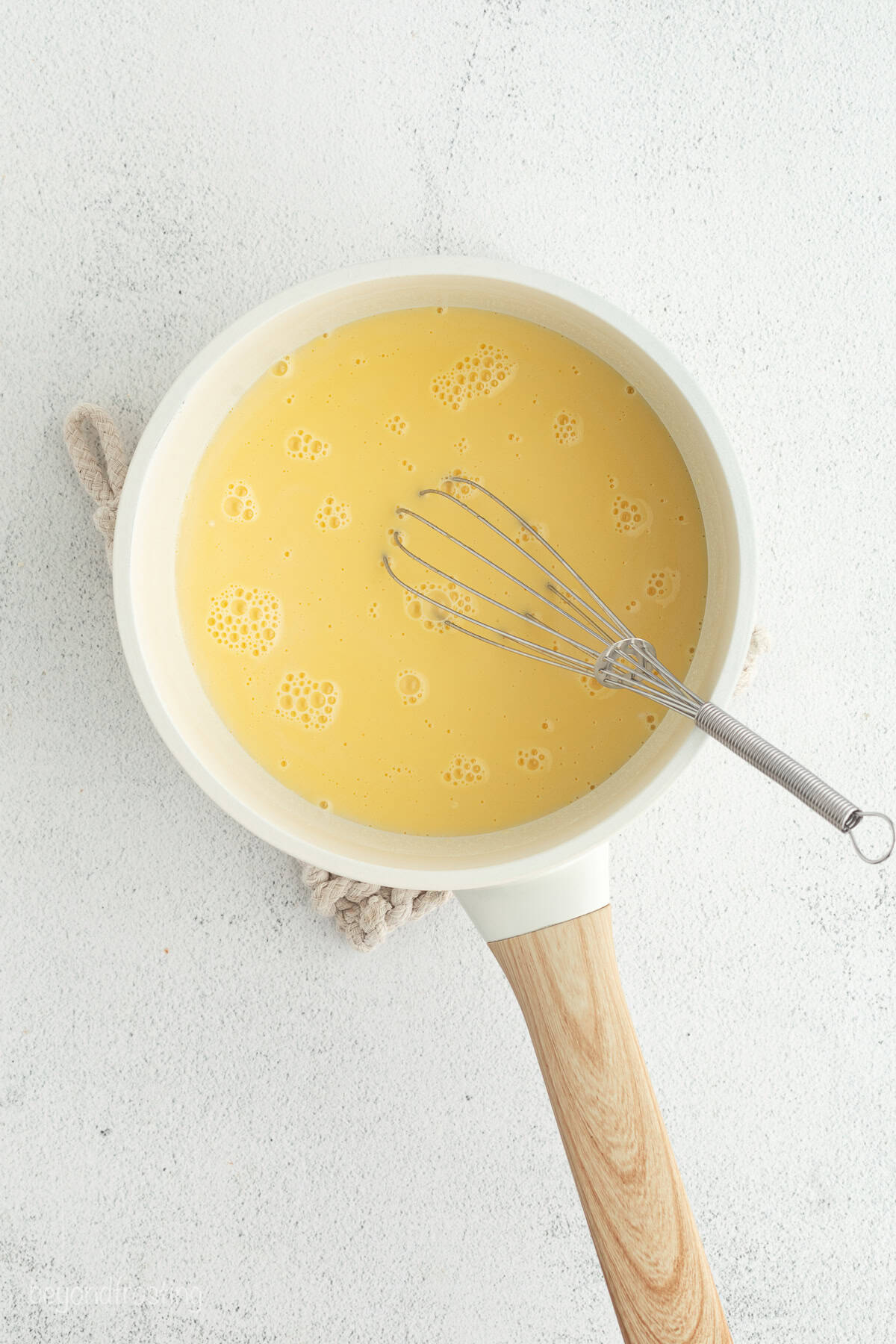 Make the best no-bake banana pudding cheesecake with creamy cheesecake filling, fresh banana slices, homemade pudding, and whipped cream. Pudding in a saucepan with a whisk.