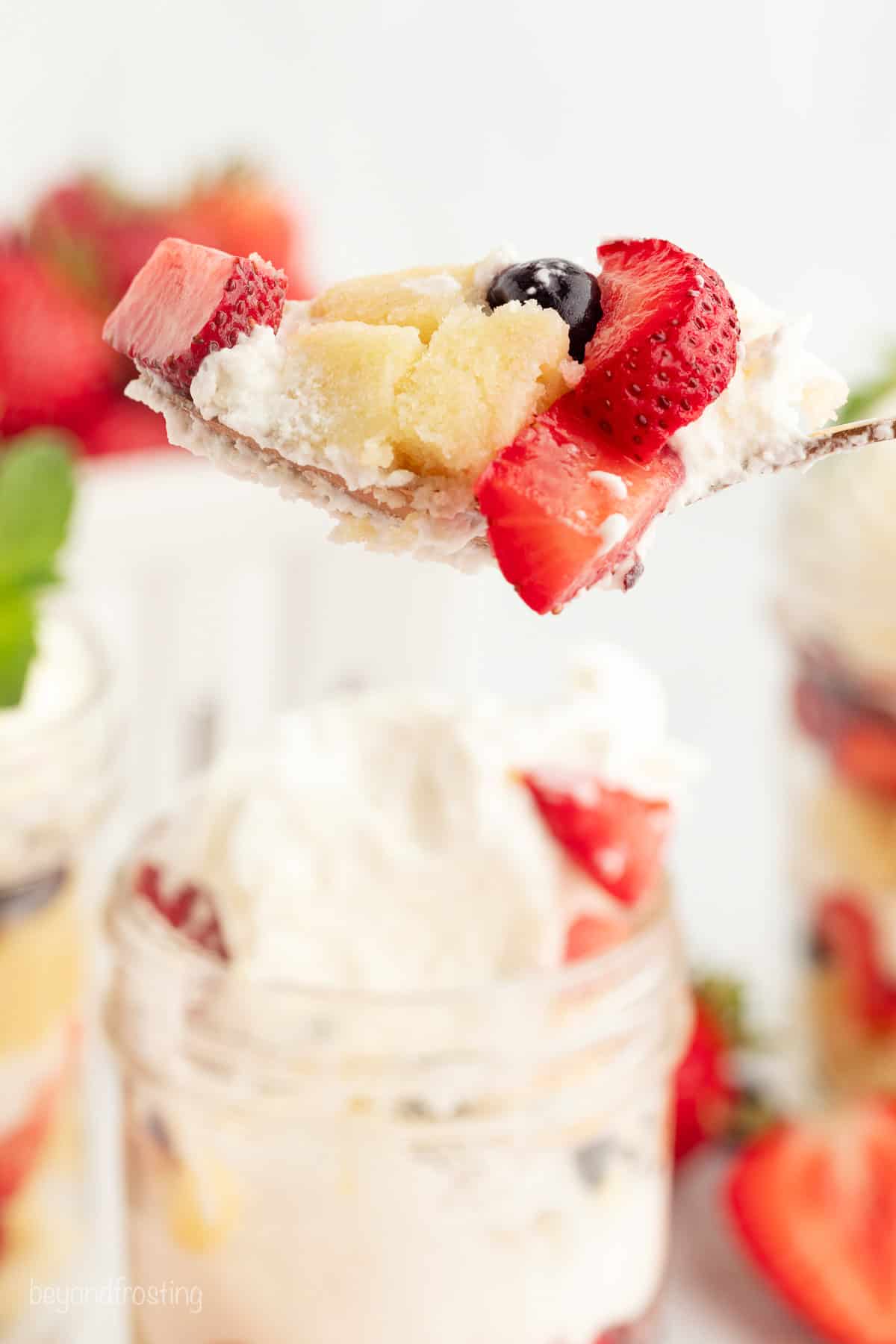 Mini trifles layer homemade pound cake, juicy berries, and mascarpone whipped cream into jars, parfait-style. Great for parties and holidays! A spoon lifting a bite of berry trifle from a jar.