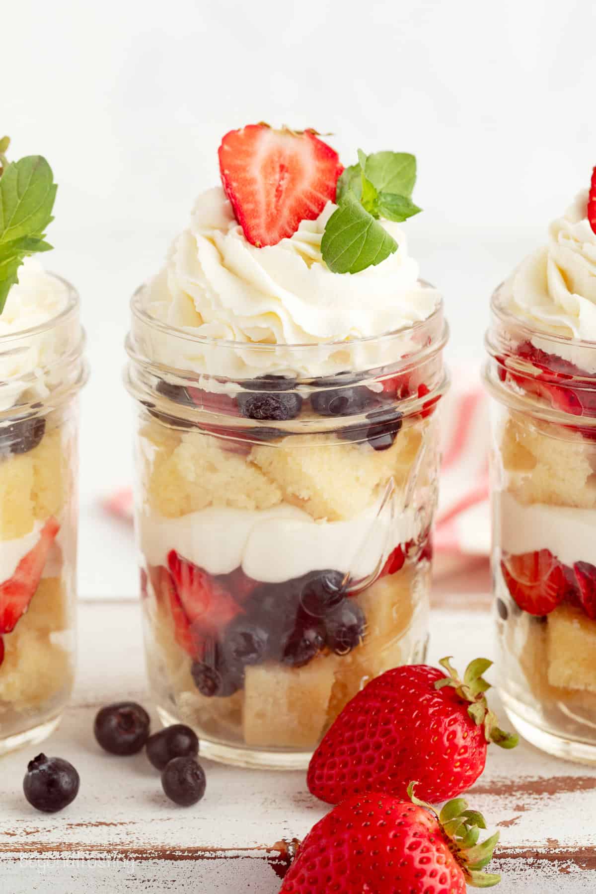 Mini trifles layer homemade pound cake, juicy berries, and mascarpone whipped cream into jars, parfait-style. Great for parties and holidays! Mini trifles served parfait-style in jars with layers of pound cake, macerated berries, and whipped cream.
