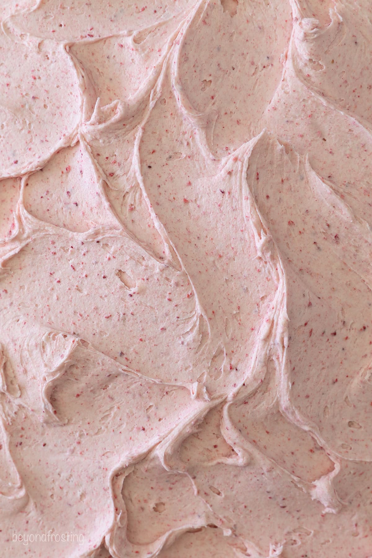 This strawberry crunch cake is a moist vanilla cake topped with creamy strawberry frosting and a crunchy strawberry and Golden Oreo crumb. Close up of strawberry frosting spread over a cooled vanilla cake.