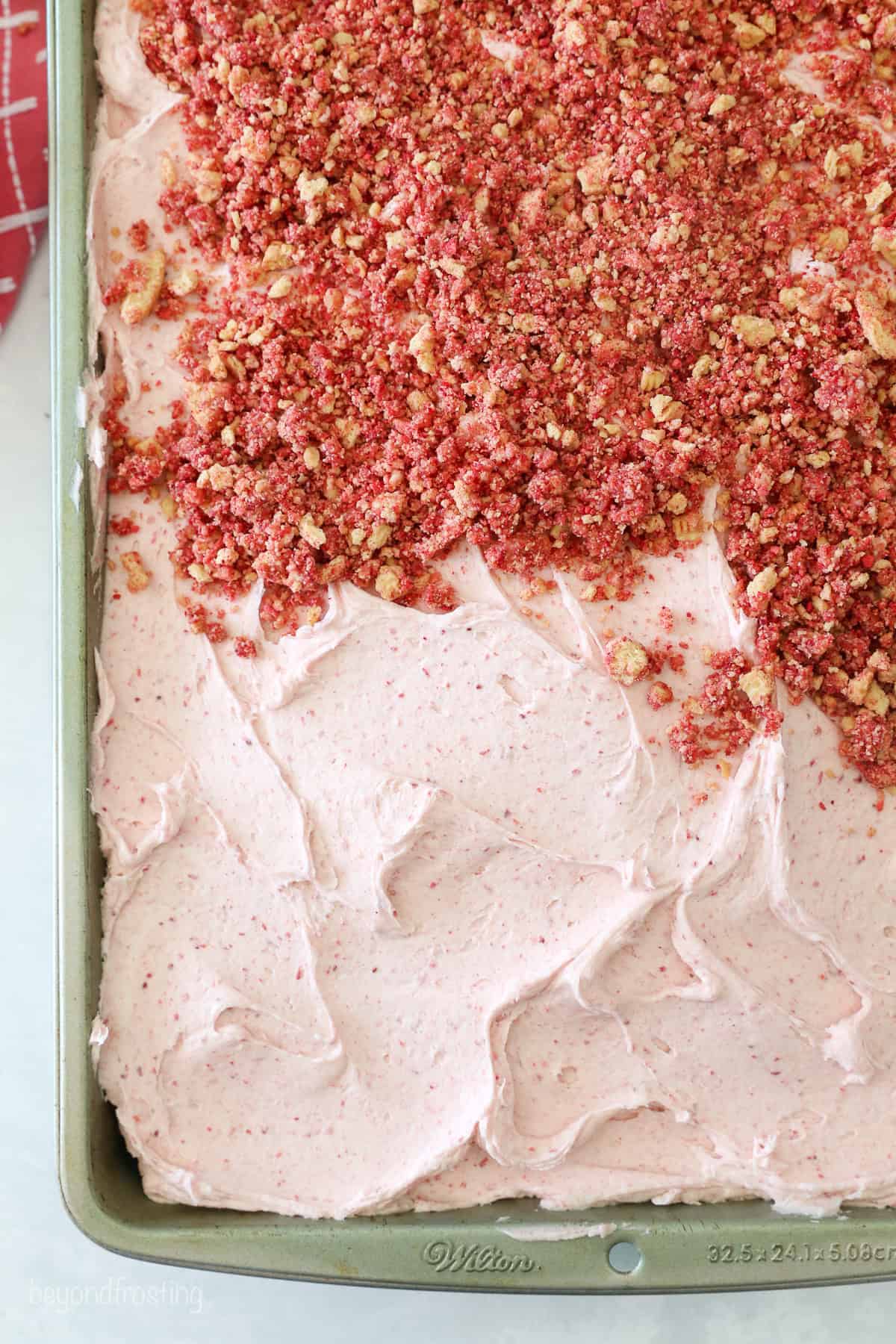 This strawberry crunch cake is a moist vanilla cake topped with creamy strawberry frosting and a crunchy strawberry and Golden Oreo crumb. Strawberry crunch spread on top of a cake frosted with strawberry frosting.