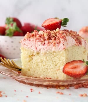 A slice of strawberry crunch cake with strawberry frosting, topped with a fresh strawberry on a plate.