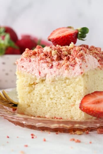 A slice of strawberry crunch cake with strawberry frosting, topped with a fresh strawberry on a plate.