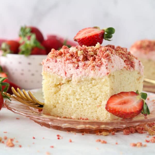 A slice of strawberry crunch cake with strawberry frosting, topped with a fresh strawberry on a plate.