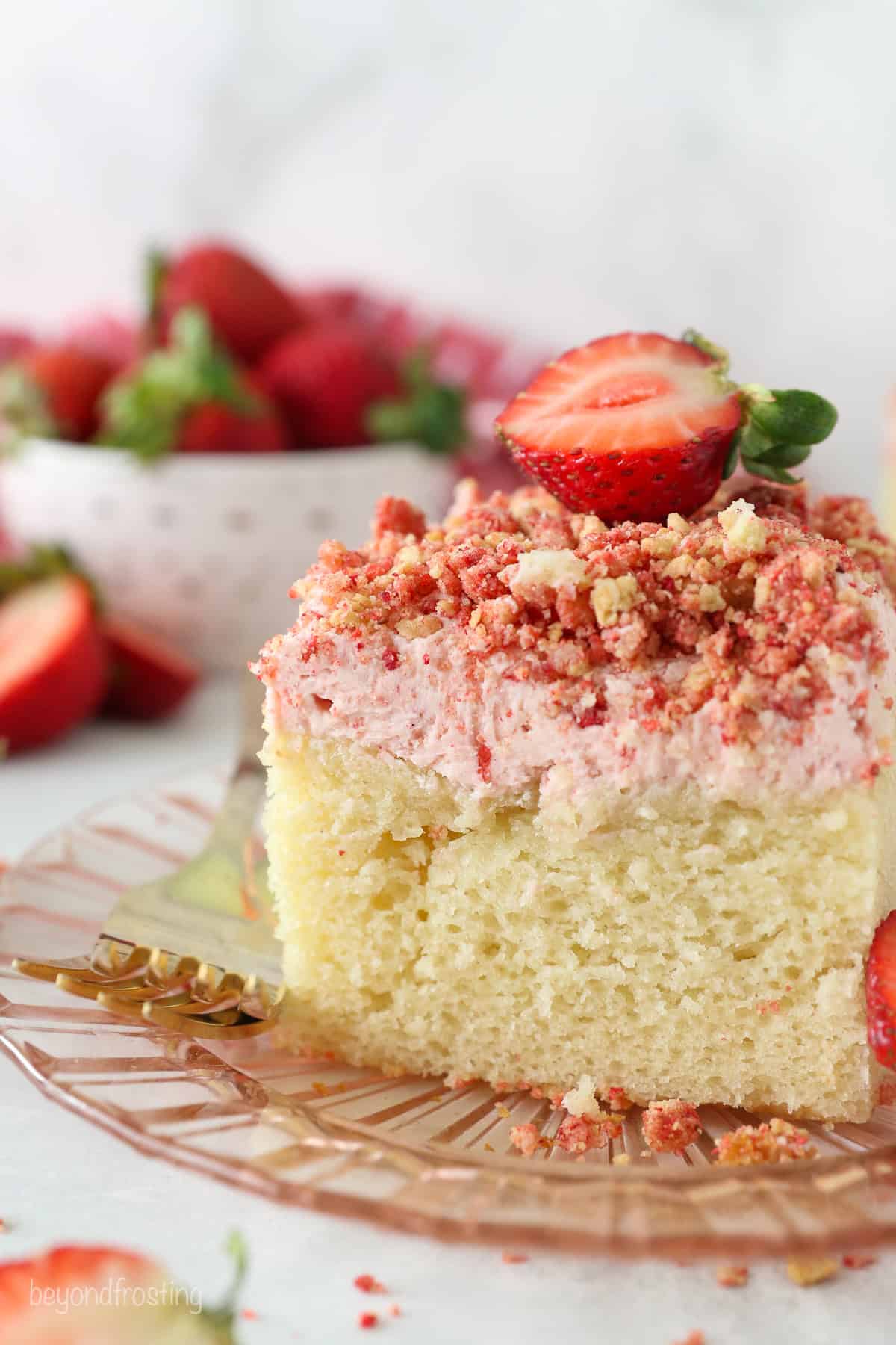 This strawberry crunch cake is a moist vanilla cake topped with creamy strawberry frosting and a crunchy strawberry and Golden Oreo crumb. A slice of strawberry crunch cake with strawberry frosting, topped with a fresh strawberry on a plate.