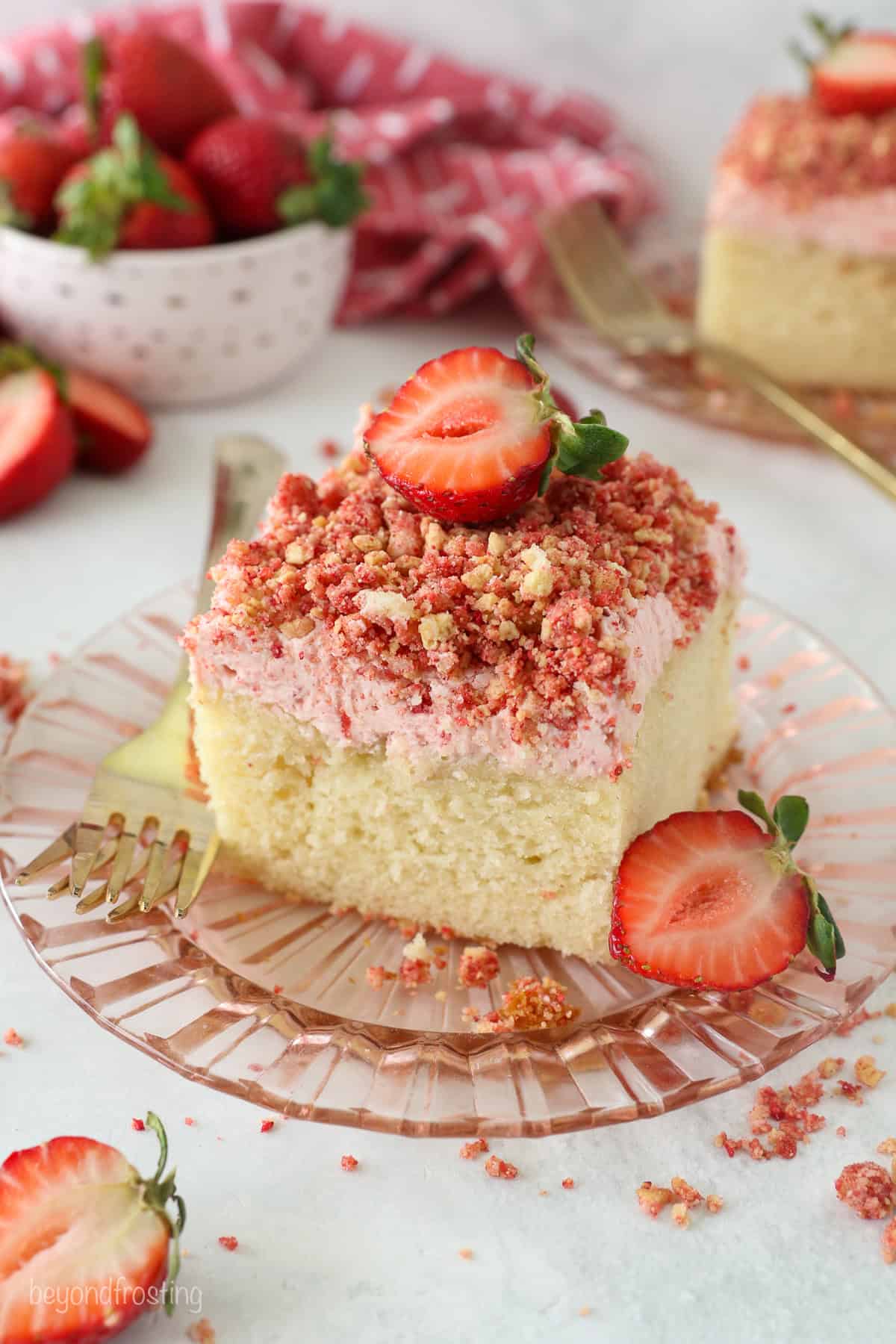 This strawberry crunch cake is a moist vanilla cake topped with creamy strawberry frosting and a crunchy strawberry and Golden Oreo crumb. A slice of strawberry crunch cake topped with a fresh strawberry on a plate.