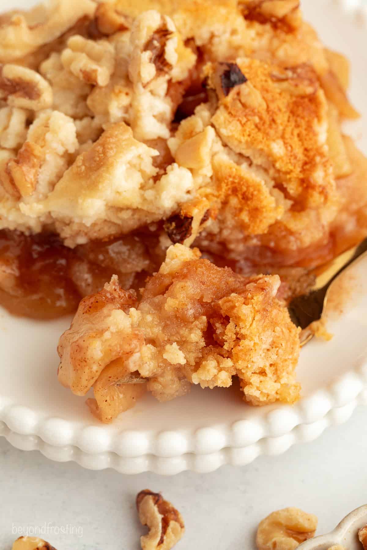 You don't need to stir this cozy apple dump cake! Dump juicy cinnamon apples into a cake pan, top with dry cake mix and butter, and bake. Close up of a serving of apple dump cake with a forkful on a plate.
