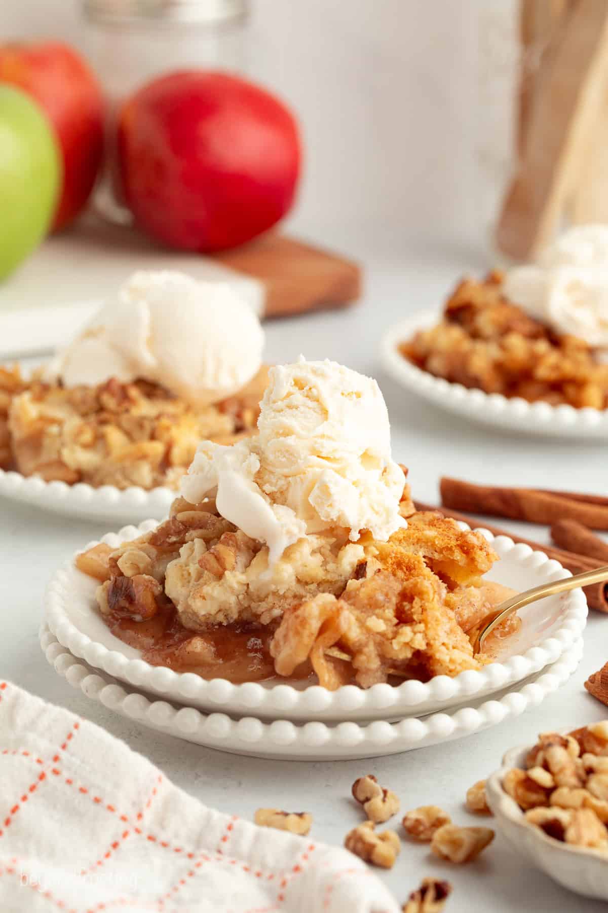 You don't need to stir this cozy apple dump cake! Dump juicy cinnamon apples into a cake pan, top with dry cake mix and butter, and bake. A serving of apple dump cake topped with vanilla ice cream on a plate.