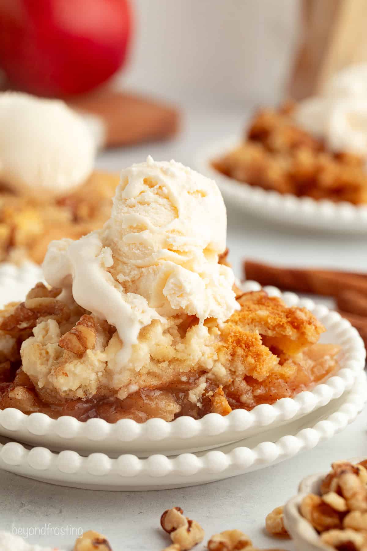 You don't need to stir this cozy apple dump cake! Dump juicy cinnamon apples into a cake pan, top with dry cake mix and butter, and bake. A serving of apple dump cake topped with vanilla ice cream on a plate.