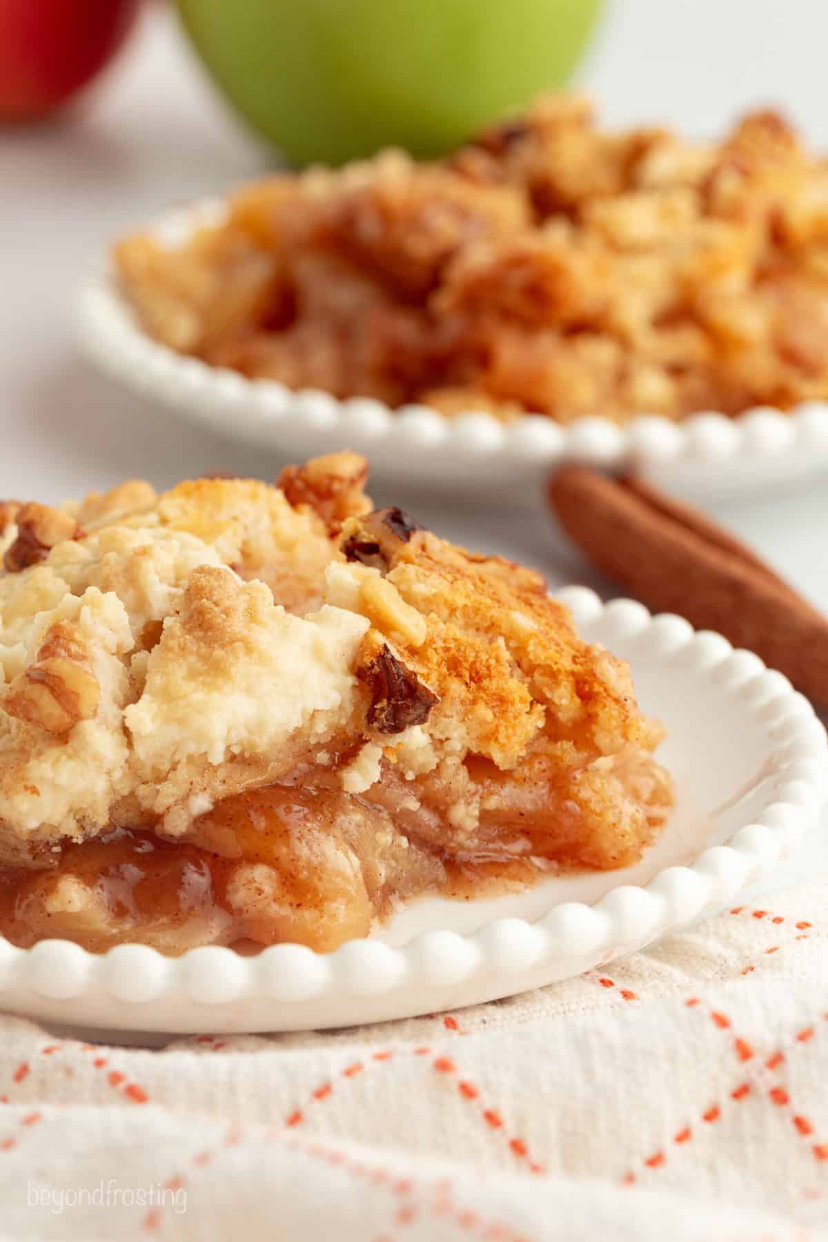 You don't need to stir this cozy apple dump cake! Dump juicy cinnamon apples into a cake pan, top with dry cake mix and butter, and bake. A serving of apple dump cake on a plate.