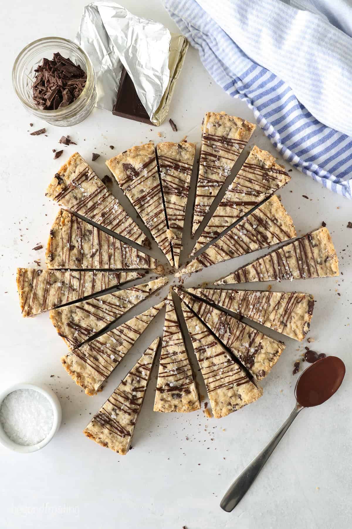 These classic, buttery shortbread cookies are filled with chopped chocolate and topped with a chocolate drizzle. Perfect for holiday baking! Overhead view of chocolate chip shortbread cookies cut into wedges and drizzled with chocolate.