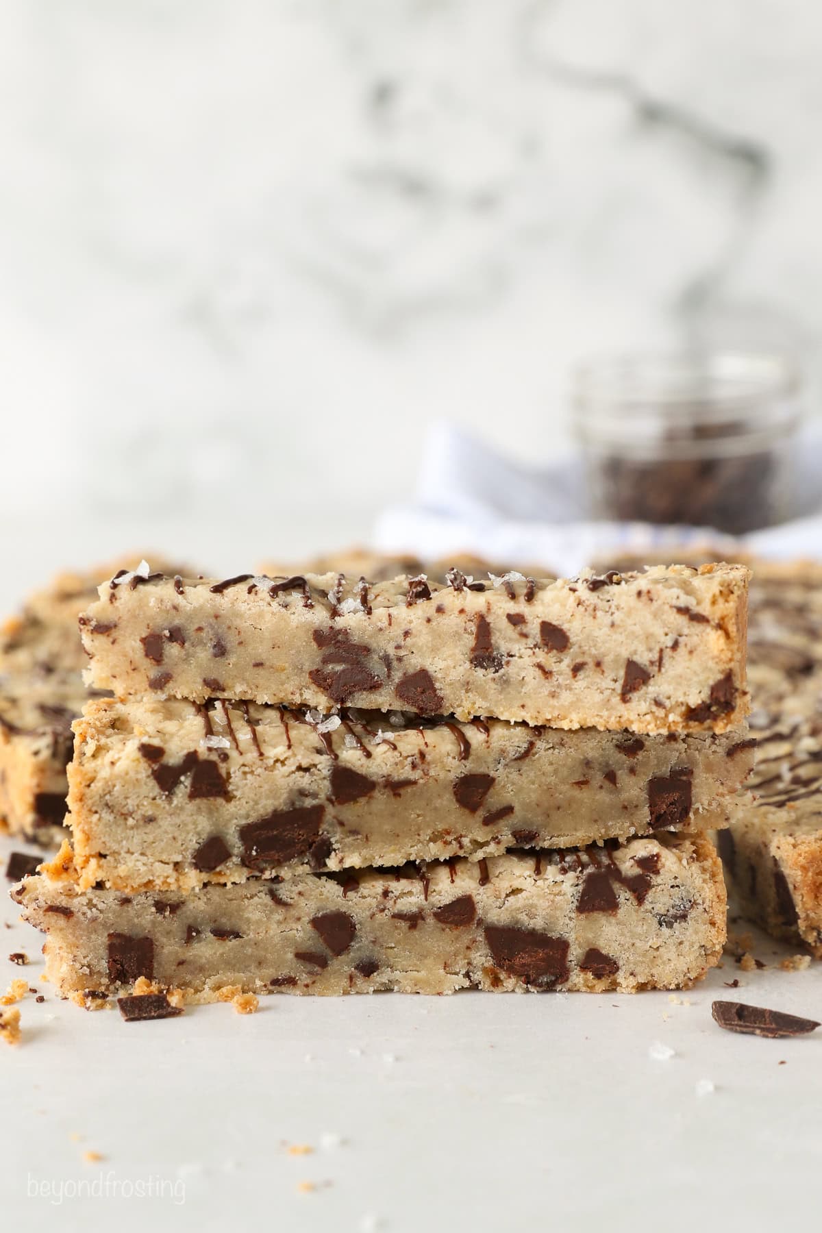 These classic, buttery shortbread cookies are filled with chopped chocolate and topped with a chocolate drizzle. Perfect for holiday baking! Side view of three buttery chocolate chip shortbread cookies stacked.