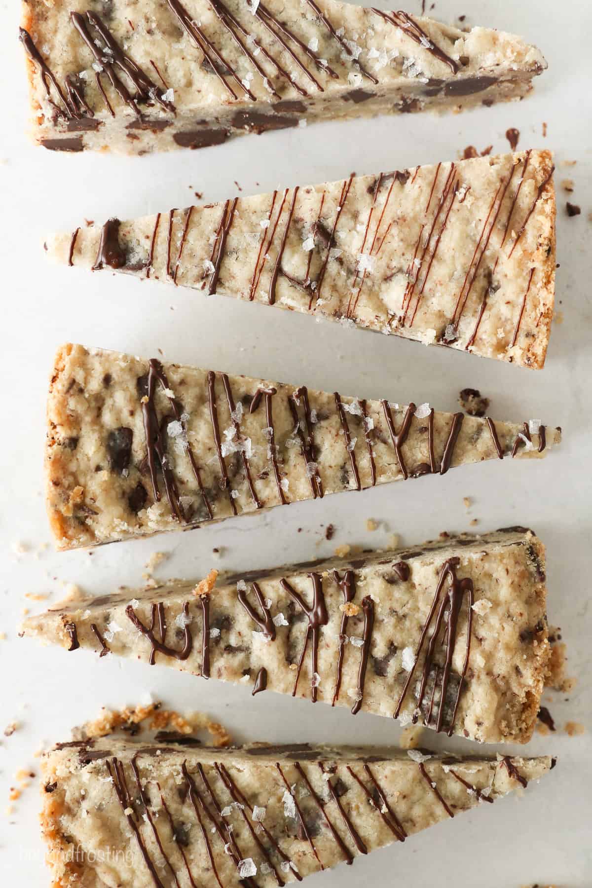 These classic, buttery shortbread cookies are filled with chopped chocolate and topped with a chocolate drizzle. Perfect for holiday baking! Overhead view of chocolate chip shortbread cookies cut into wedges and drizzled with chocolate.