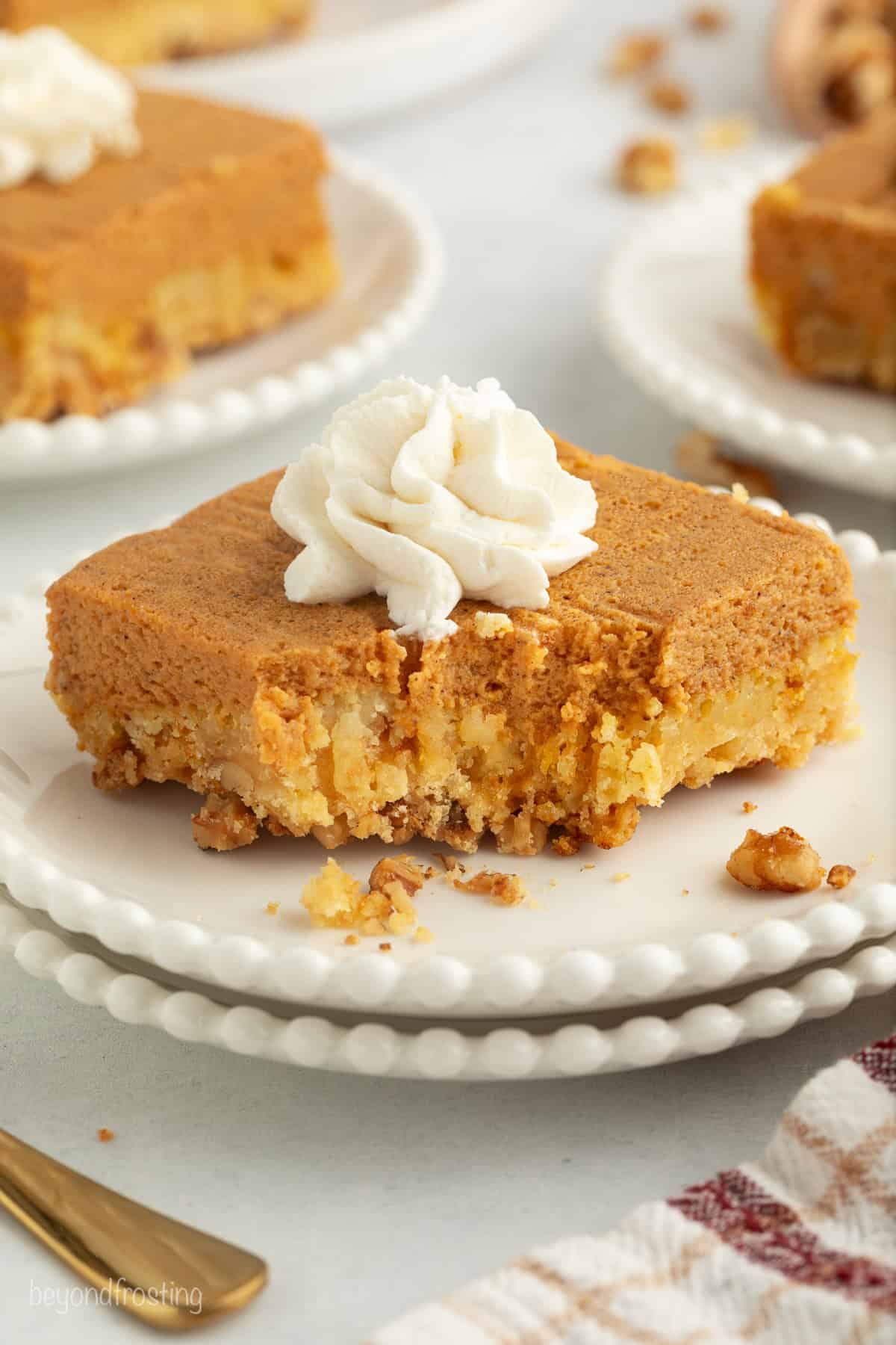 Fall pumpkin crunch cake is an easy, dump cake-style dessert with rich pumpkin filling and a buttery, crunchy cake mix layer with walnuts. A slice of pumpkin crunch cake topped with whipped cream, with a forkful missing from the corner.