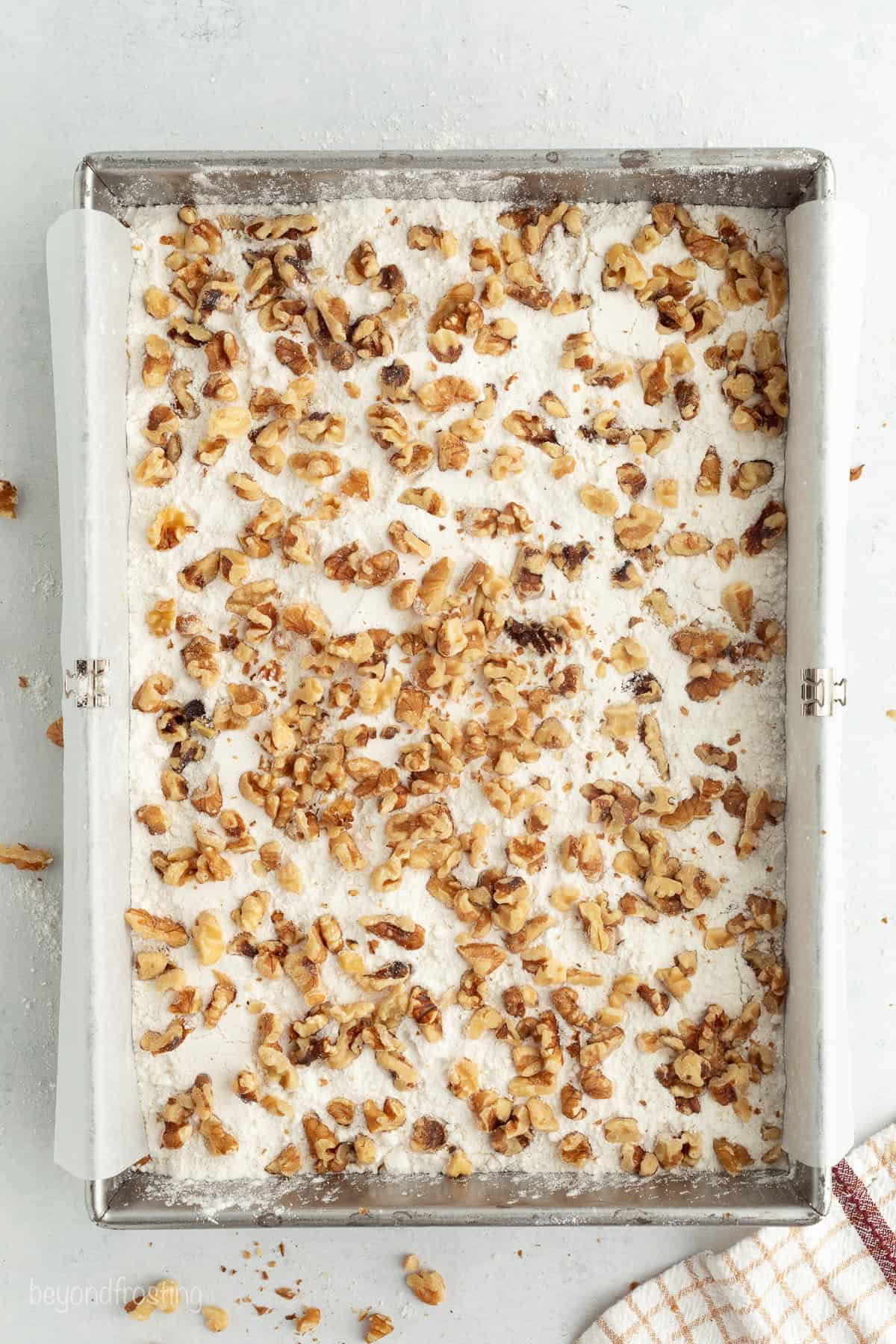 Fall pumpkin crunch cake is an easy, dump cake-style dessert with rich pumpkin filling and a buttery, crunchy cake mix layer with walnuts. Chopped walnuts scattered in the bottom of a baking pan.