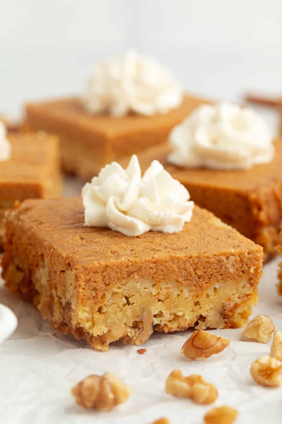 Fall pumpkin crunch cake is an easy, dump cake-style dessert with rich pumpkin filling and a buttery, crunchy cake mix layer with walnuts. Slices of pumpkin crunch cake topped with whipped cream on a plate.