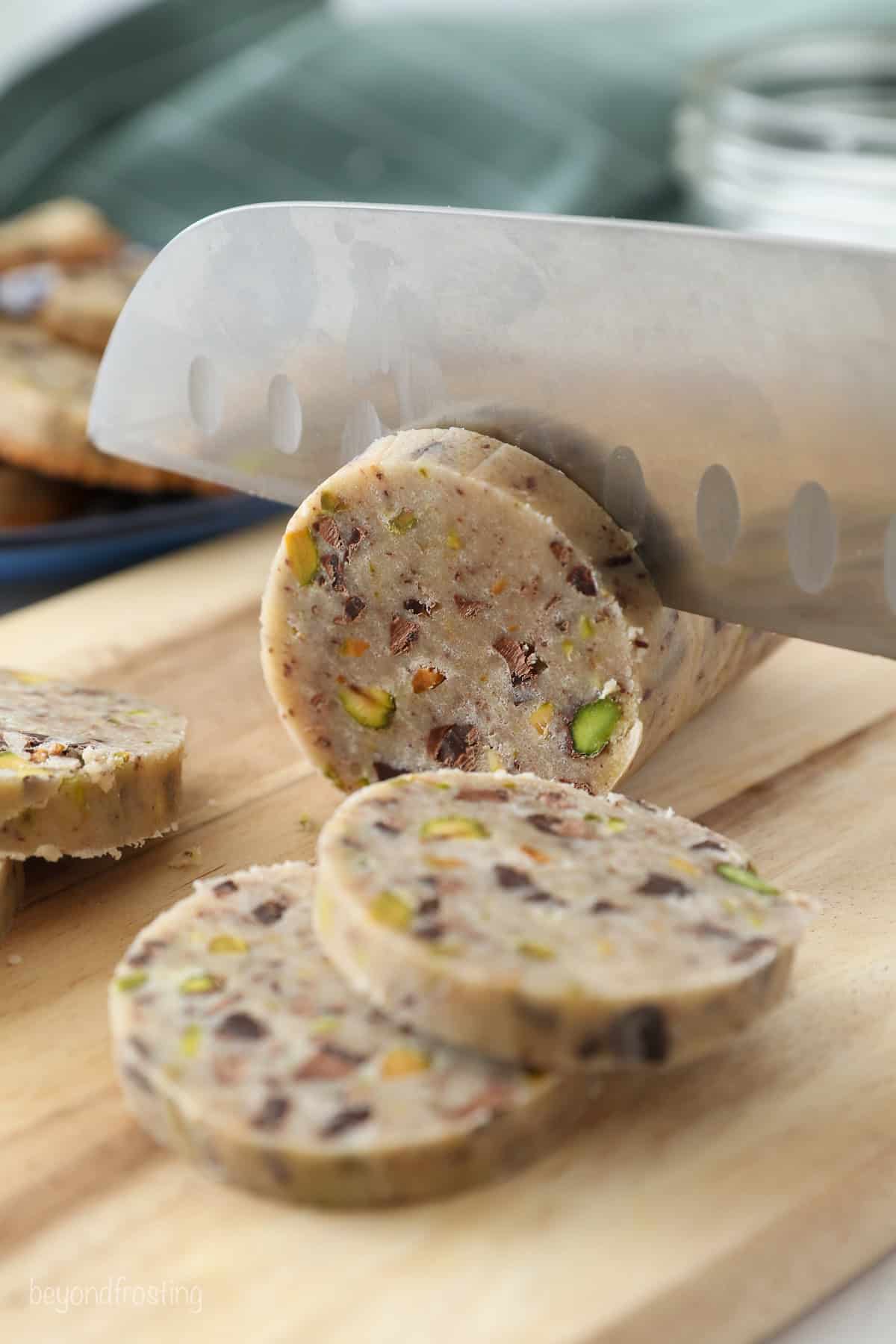 Using a large sharp knife to slice the chilled shortbread cookie dough log on a cutting board.