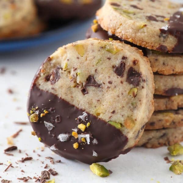 Close up of a chocolate-dipped pistachio shortbread cookie propped up against a stack of cookies.