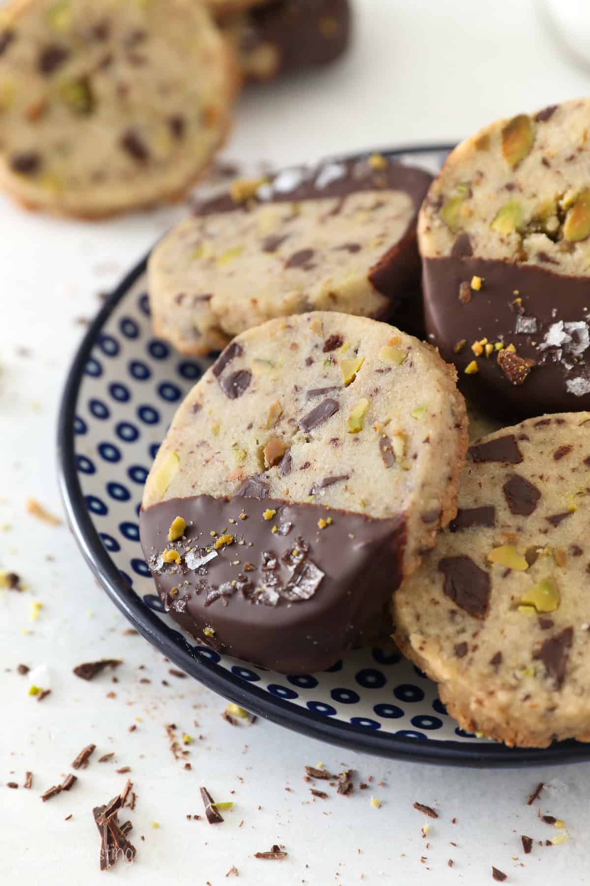 Close up of chocolate-dipped pistachio shortbread cookies piled on a plate.